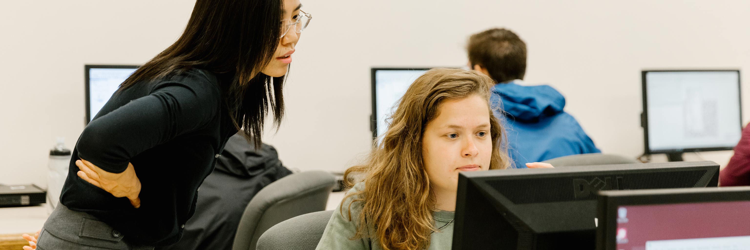 Instructor helping a student at a computer workstation 