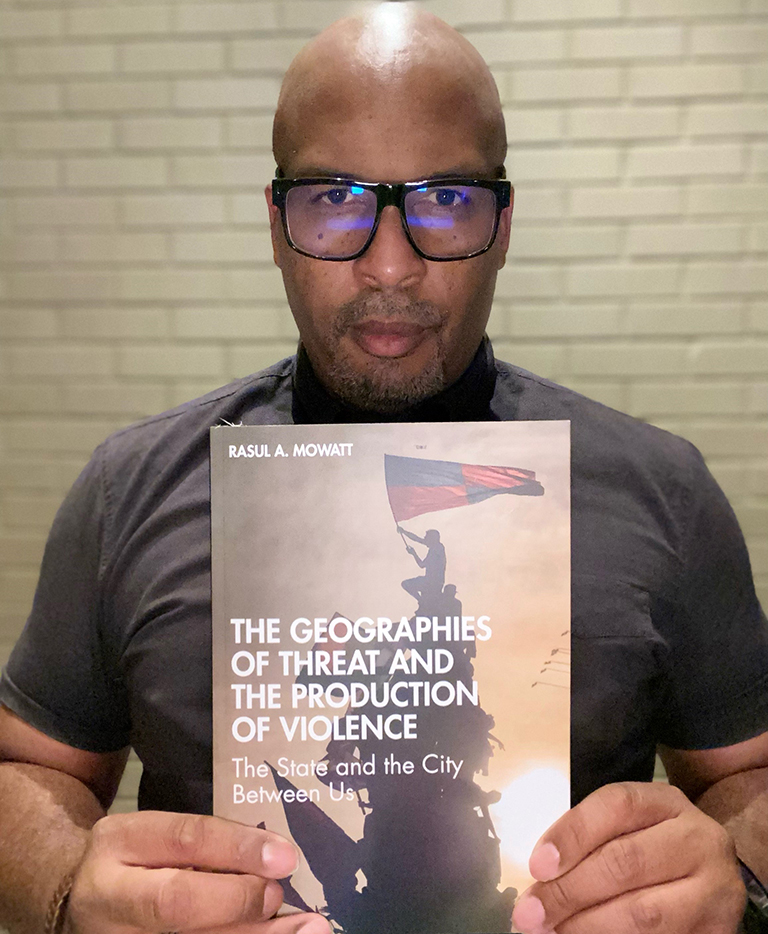 Dr. Rasul Mowatt holding his book, The Geographies of Threat and the Production of Violence.